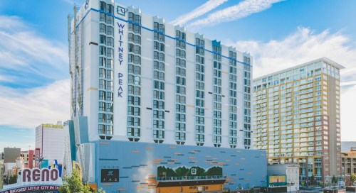 A tall hotel building with "Whitney Peak" signage, set against a clear blue sky and nearby cityscape.
