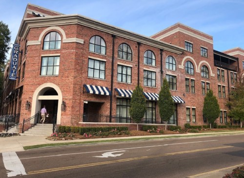 A brick building with large windows and striped awnings, featuring a sign that reads "Graduate." Trees line the entrance.
