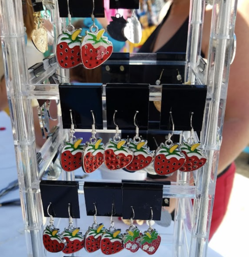 Colorful strawberry-shaped earrings displayed on a clear stand at a market.