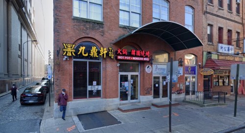 Street view of a brick building with signs for a hot pot restaurant and a Korean BBQ, with pedestrians nearby.