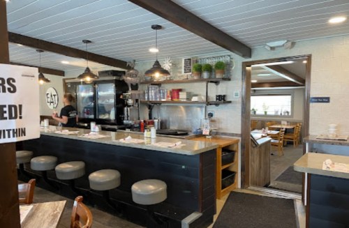 Interior of a cozy diner with a counter, seating area, and a sign indicating "Takeout Only."