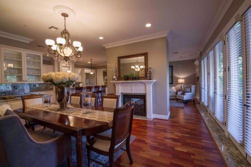 A spacious dining area with a wooden table, elegant chairs, and a fireplace, leading to a cozy living room with large windows.
