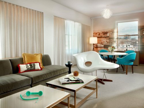 Modern living room featuring a sofa, unique chair, dining area, and stylish decor with large windows and soft lighting.