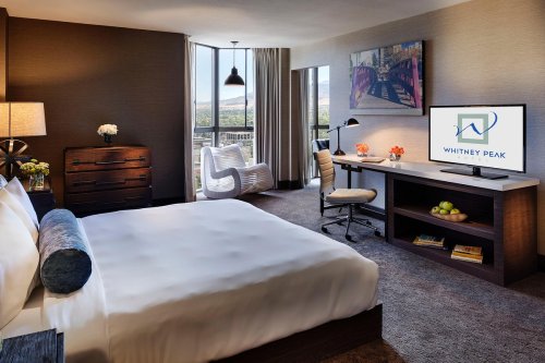 Modern hotel room featuring a king bed, desk, TV, and a view of the outdoors through large windows.