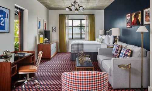 A stylish hotel room featuring a bed, seating area, desk, and modern decor with a mix of patterns and colors.