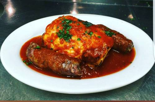 A plate of meatloaf topped with tomato sauce, accompanied by two sausage links, garnished with parsley.