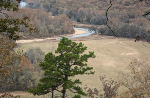 A winding river flows through a wooded landscape with autumn foliage and an open field in the foreground.