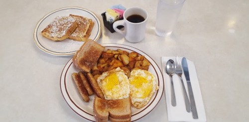 A breakfast plate with eggs, sausage, toast, and home fries, alongside a cup of coffee and a glass of water.