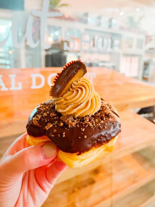 A hand holding a chocolate-covered donut topped with peanut butter frosting and a mini peanut butter cup.