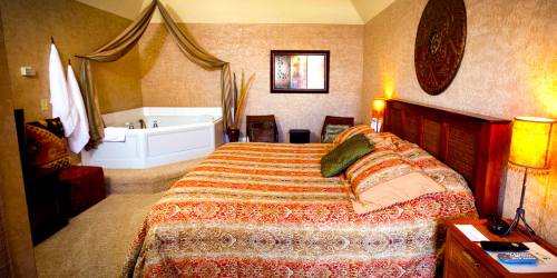 Cozy bedroom with a patterned bedspread, a jacuzzi tub, and warm lighting, creating a relaxing atmosphere.