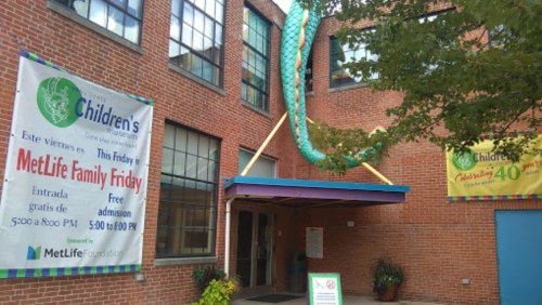 Entrance of a children's museum with banners for MetLife Family Friday and a large green dragon decoration.