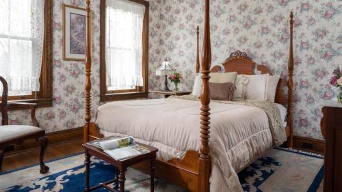 Cozy bedroom with a four-poster bed, floral wallpaper, and a small table beside a window with soft natural light.