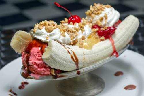 A banana split topped with whipped cream, nuts, cherries, and various ice cream flavors in a silver dish.