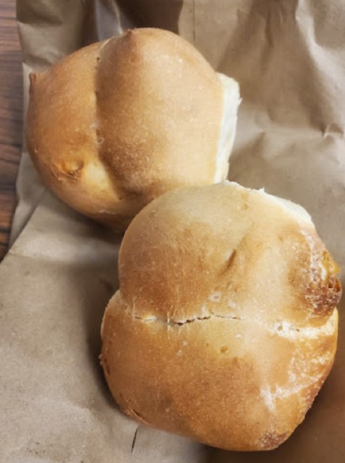 Two freshly baked rolls resting on a piece of brown paper.