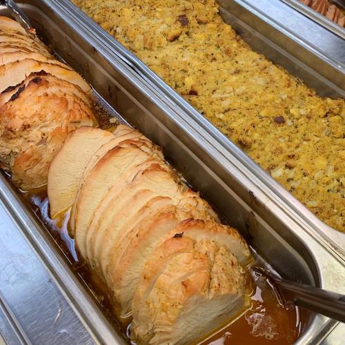Sliced turkey in gravy next to a tray of stuffing, both served in stainless steel containers.