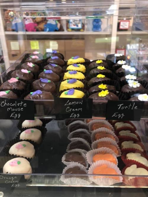 A display of assorted chocolates, including Chocolate Mousse, Lemon Cream, and Turtle, in a glass case.