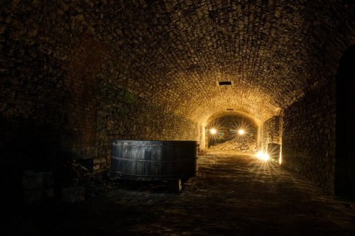 A dimly lit stone tunnel with a barrel and soft lights illuminating the walls.