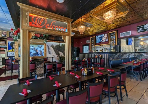 Interior of a restaurant featuring a "Welcome" sign, elegant decor, tables set with red napkins, and a bar area.
