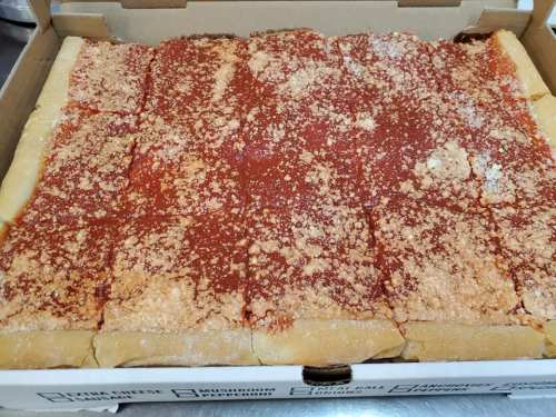 A pizza in a box, topped with tomato sauce and a sprinkle of cheese, cut into rectangular slices.