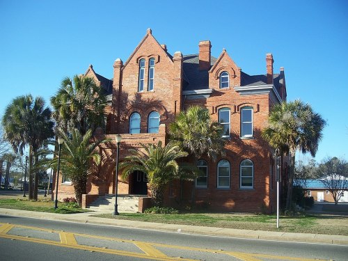 Historic red brick building with palm trees in front, set against a clear blue sky.