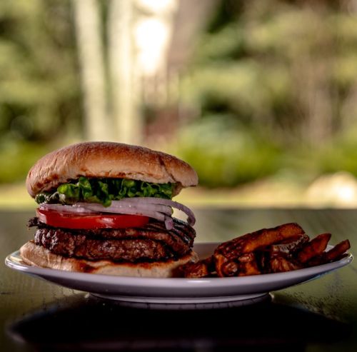 A juicy hamburger with lettuce, tomato, and onion, served with sweet potato fries on a white plate.