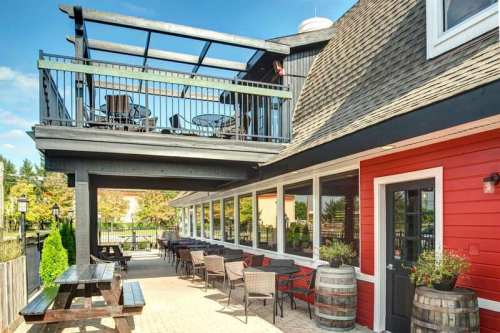 A cozy restaurant exterior featuring a red wall, outdoor seating, and a balcony with tables under a clear blue sky.