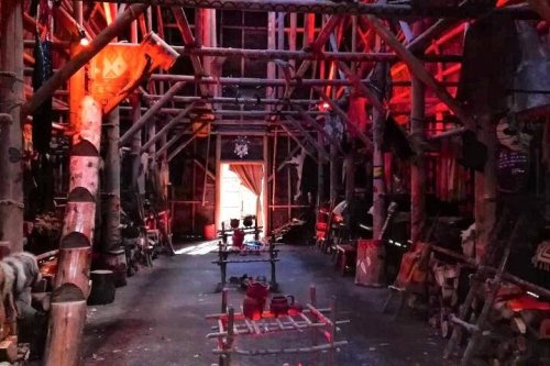 Interior of a rustic wooden structure with red lighting, featuring tables and various tools and decorations.