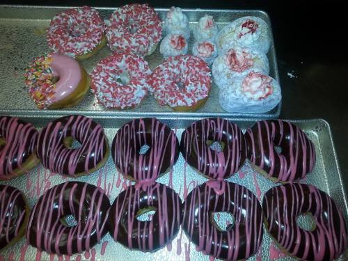 A tray of assorted donuts: pink frosted, sprinkled, and chocolate glazed with pink drizzle.