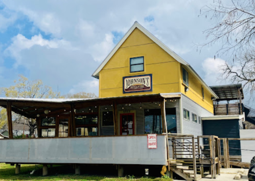 A yellow two-story building with a sign reading "Johnson's" and a deck, surrounded by trees and a blue sky.