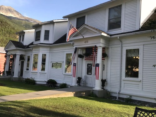 A white house with American flags, surrounded by greenery and mountains in the background.