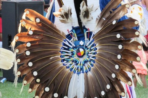 A colorful feathered headdress with a circular design, featuring beads and a central emblem, displayed outdoors.