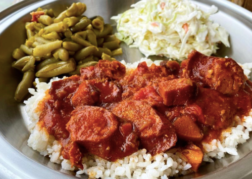 A metal plate with rice topped with meat in sauce, served with green beans and coleslaw on the side.