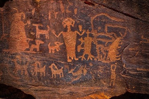 Ancient rock art depicting human figures and animals, showcasing intricate petroglyphs on a stone surface.