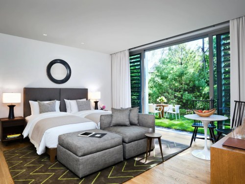 A modern hotel room with a bed, seating area, and large windows overlooking a garden patio.
