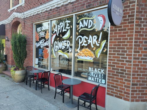 Window display featuring colorful text promoting apple and ginger pie for Thanksgiving, with outdoor seating visible.