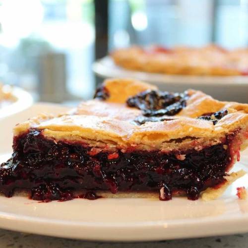 A slice of berry pie with a golden crust, revealing a rich, dark filling on a white plate.