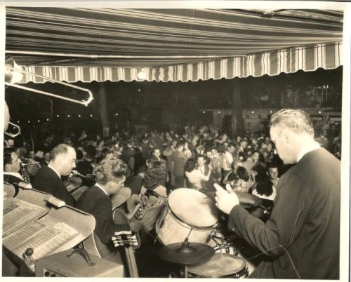 A lively dance floor filled with people, with a band performing on stage in a vintage setting.