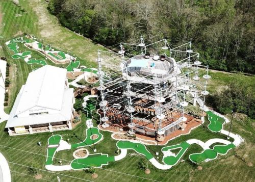 Aerial view of a mini-golf course with a multi-level adventure structure surrounded by greenery.