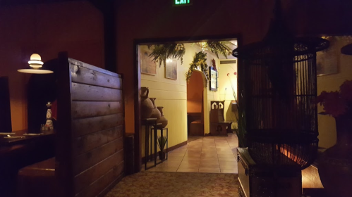 Dimly lit restaurant interior with wooden booths, a decorative birdcage, and a hallway leading to another area.