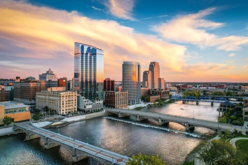 A vibrant city skyline at sunset, reflecting on a river with bridges and colorful clouds in the sky.