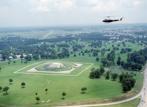 Aerial view of a large green landscape with a helicopter flying over a historic building surrounded by trees.