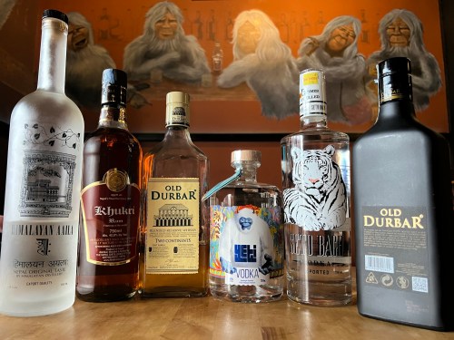 A lineup of various liquor bottles on a table, with a mural of gorillas in the background.