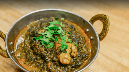 A bowl of chicken curry with spinach, garnished with fresh cilantro, served in a decorative metal dish.