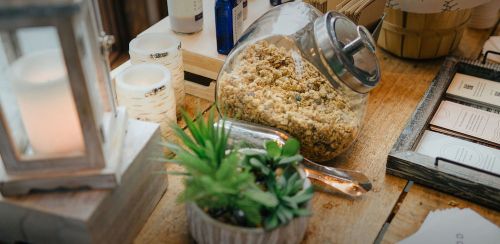 A glass jar filled with granola sits on a wooden table alongside a small plant and candles.