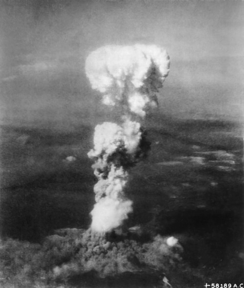 A large mushroom cloud rises from an explosion, with dark smoke billowing into the sky over a landscape.