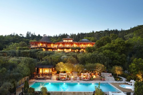 A luxurious hillside villa with a pool, surrounded by lush greenery and illuminated at dusk.