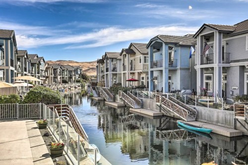 A serene canal lined with modern houses, featuring boats and lush greenery under a clear blue sky.