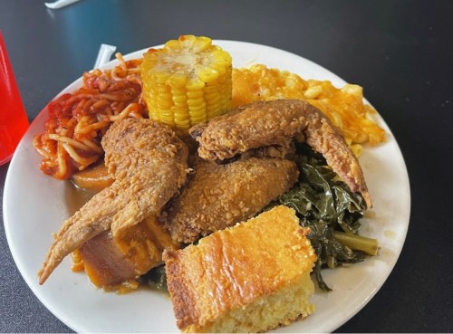 A plate of fried chicken, corn, macaroni and cheese, collard greens, spaghetti, and cornbread.