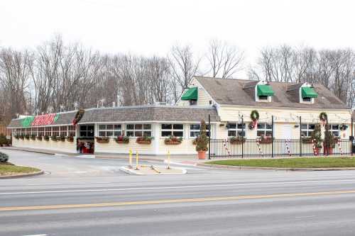 A festive restaurant with holiday decorations, featuring green awnings and potted plants, set along a road.