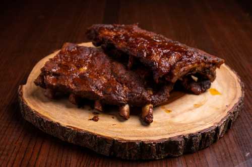 Two succulent barbecue ribs glazed with sauce, resting on a wooden serving platter.